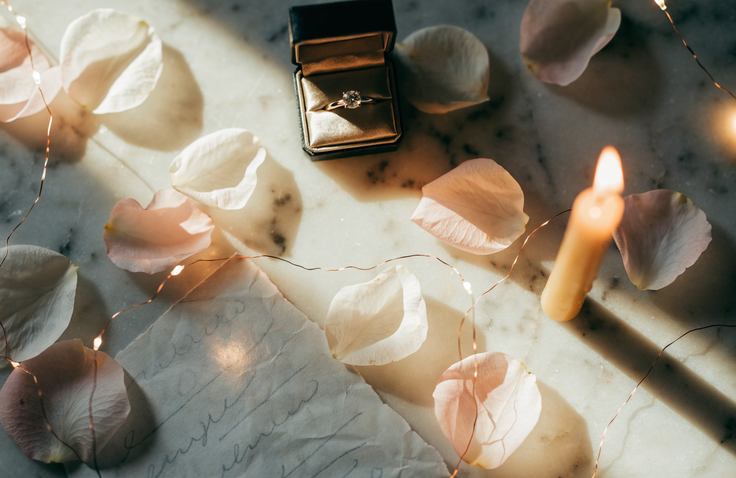 Illustrative romantic proposal flatlay with ring box, rose petals and candlelight
