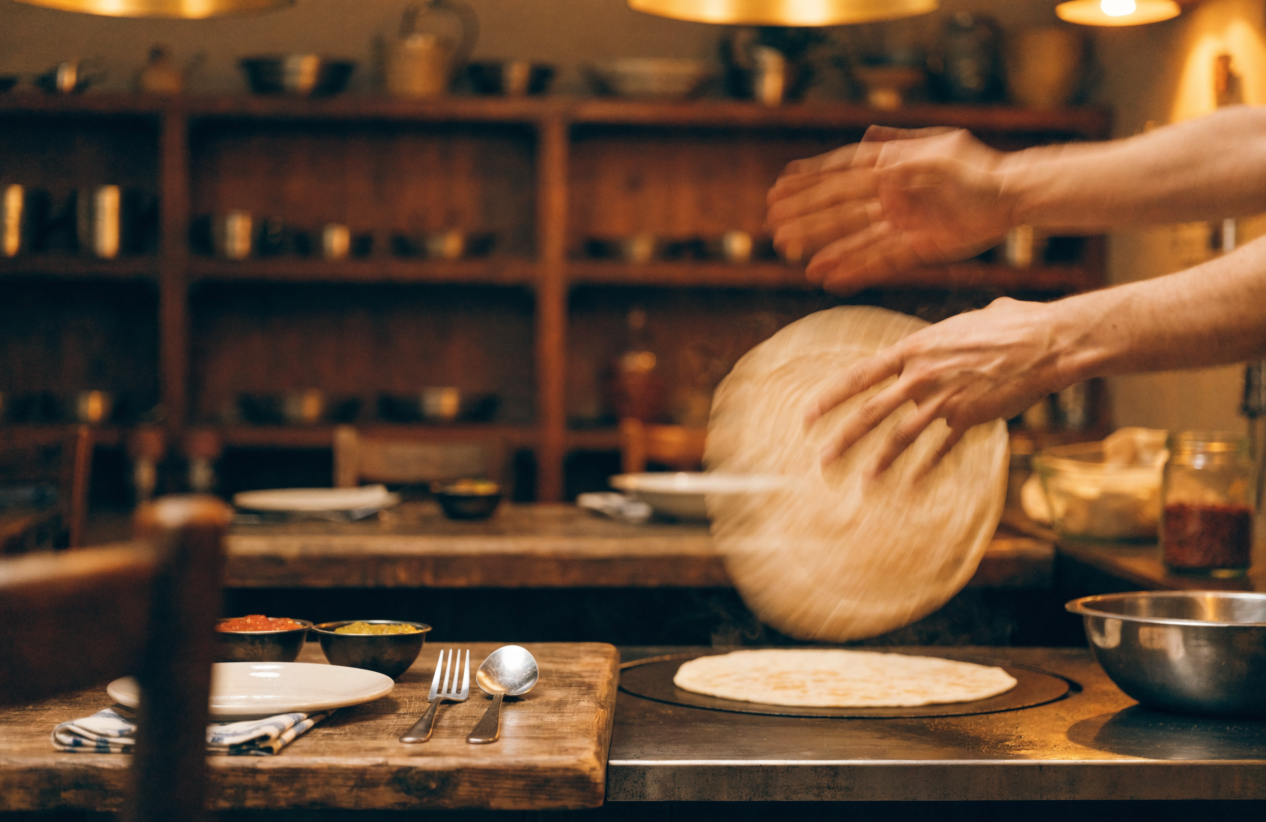 Illustrative image of hands stretching prata dough over a griddle
